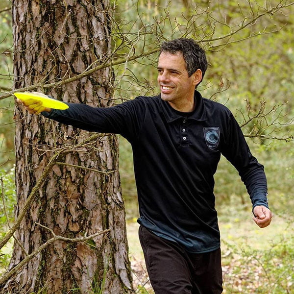 homme portant un polo noir à manches longues jouant avec un disc golf jaune dans les bois