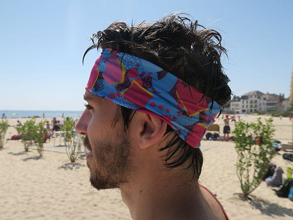 vue latérale gauche de la tête d'un homme portant un bandeau rose et bleu à la plage