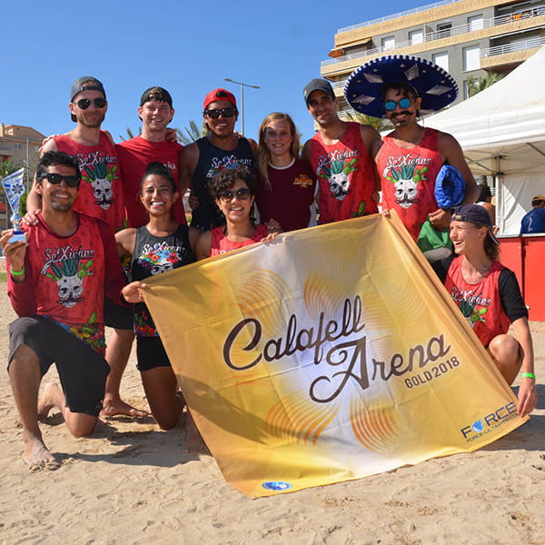 team posing on beach with red jerseys and golden flag