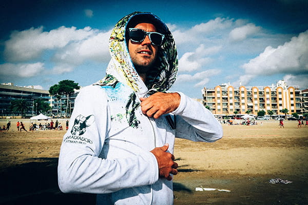man op het strand met zonnebril, gekleed in een witte gesublimeerde hoodie met capuchon omhoog