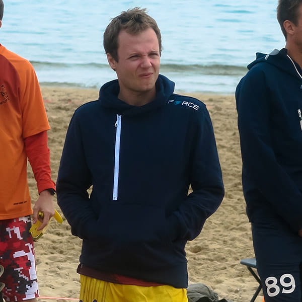 man grimacing wearing a blue hoodie on beach